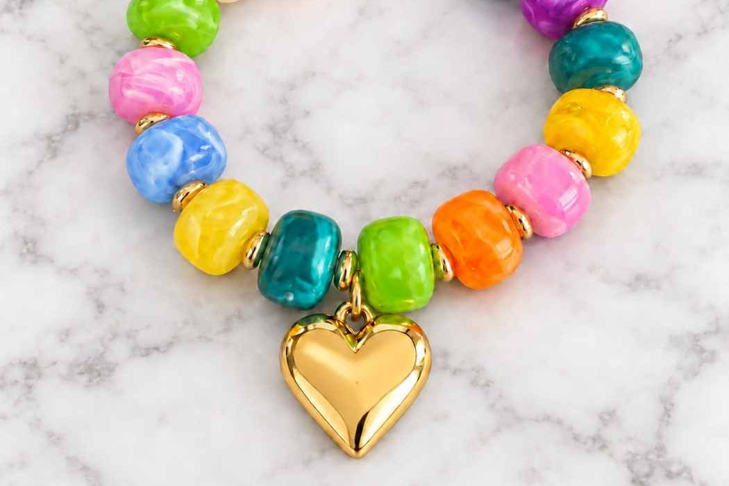 Multicolour acrylic bead bracelet with gold heart charm on a marble surface
