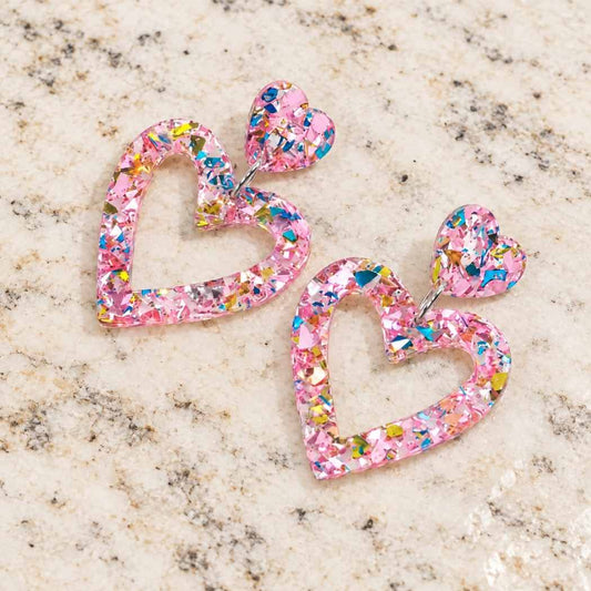 Pink glitter heart earrings displayed on granite surface