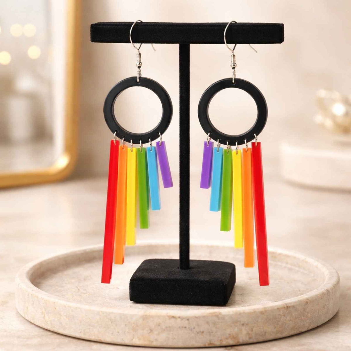 Rainbow earrings on a black stand with a blurred background